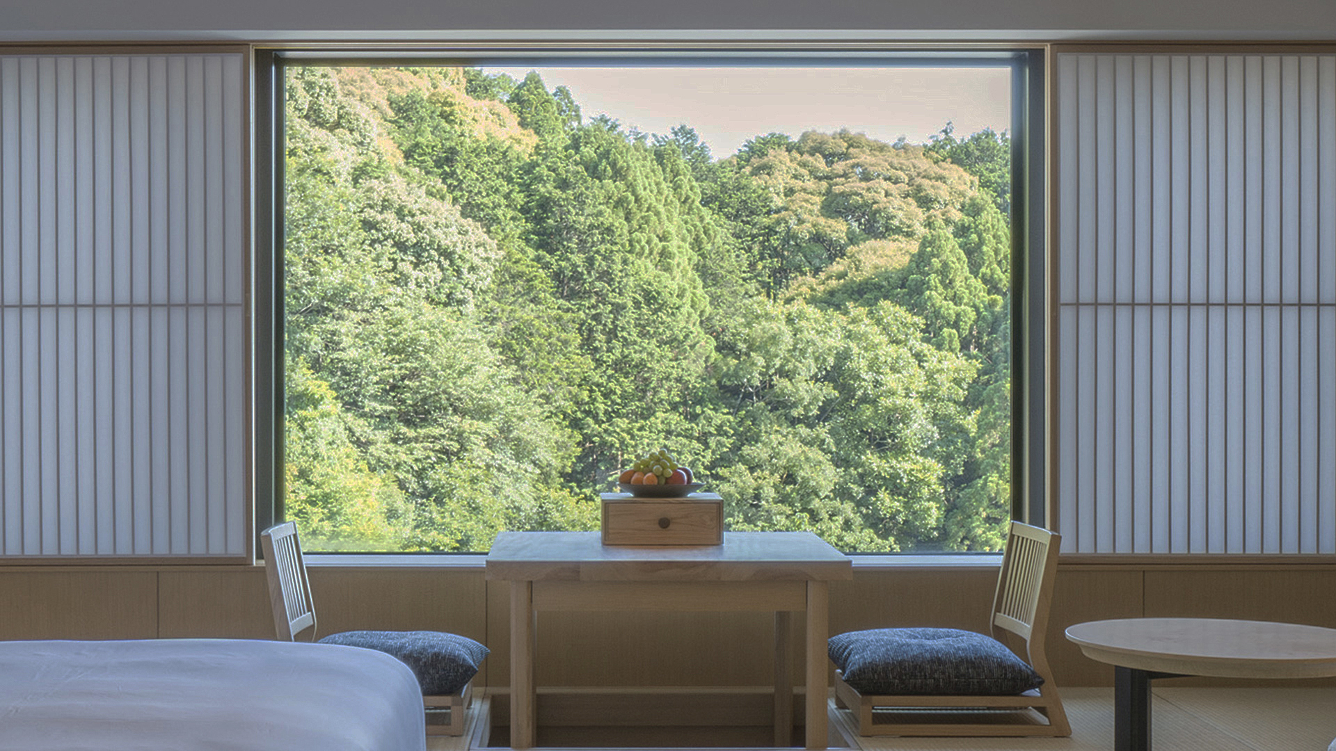 A wooden table with fruit sits by a window overlooking lush greenery at Banyan Tree Higashiyama Kyoto.